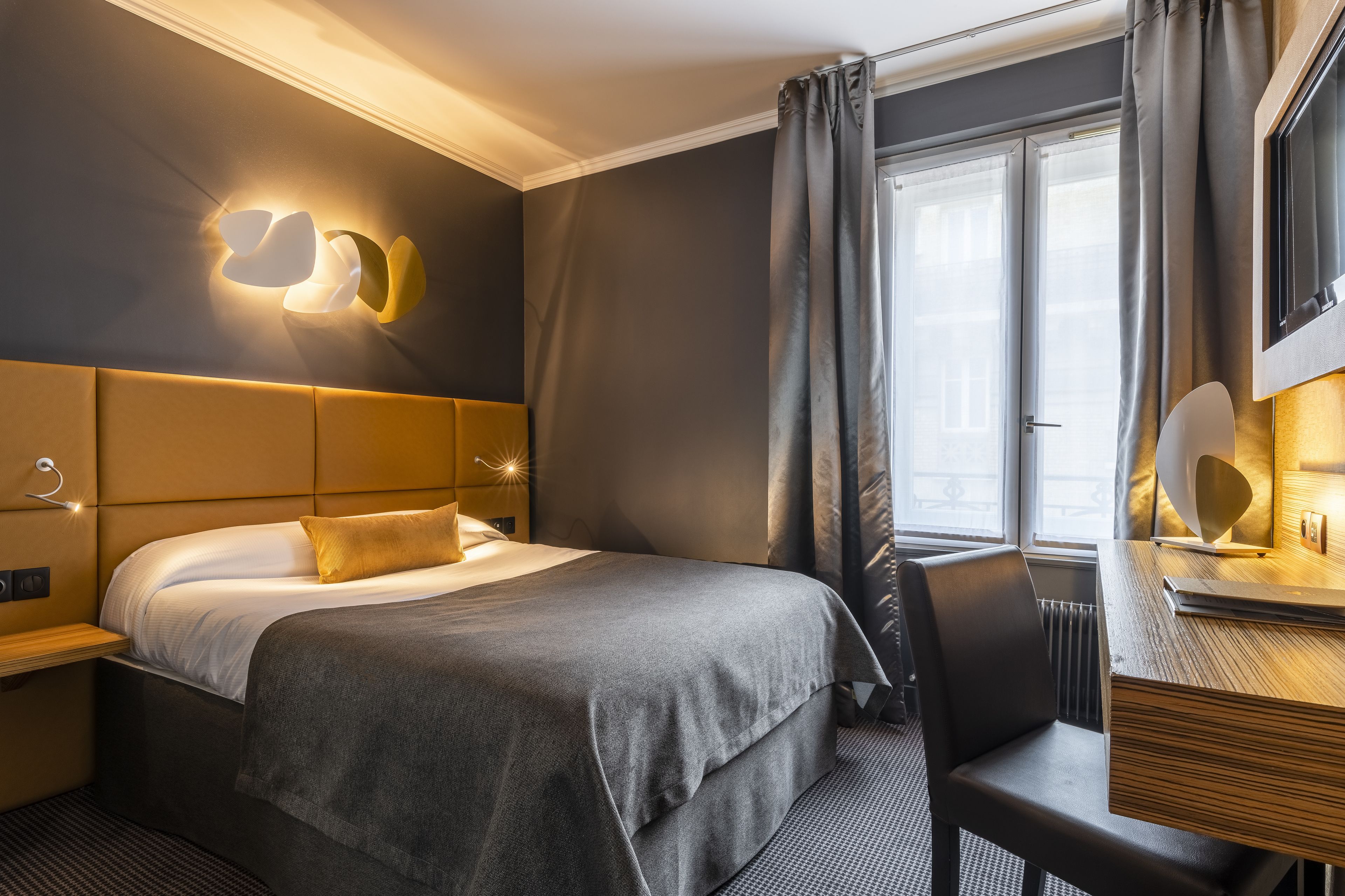 A hotel room with a bed, bedside table, and a desk with a chair.