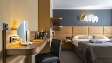 A hotel room with a modern design, featuring a large bed with a headboard, a desk with a chair, a wall-mounted lamp, and a bedside table with a lamp.