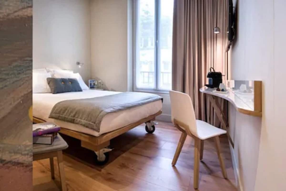 Une chambre à coucher avec un lit, une table de chevet, une chaise et une fenêtre avec des rideaux.
