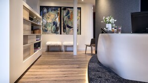 A modern reception area with a curved bench, a reception desk, and a large abstract painting on the wall. - Max Hotel (Paris)