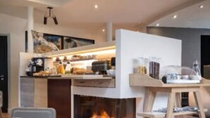 A modern kitchen with a built-in fireplace, a dining area with a round table, and a bar area with a white countertop. - Max Hotel (Paris)