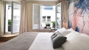 A modern hotel room with a large bed, a view of the outdoors, and a painting on the wall. - Max Hotel (Paris)