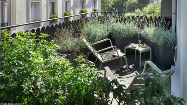 A balcony with outdoor furniture and potted plants, overlooking a cityscape. - Max Hotel (Paris)