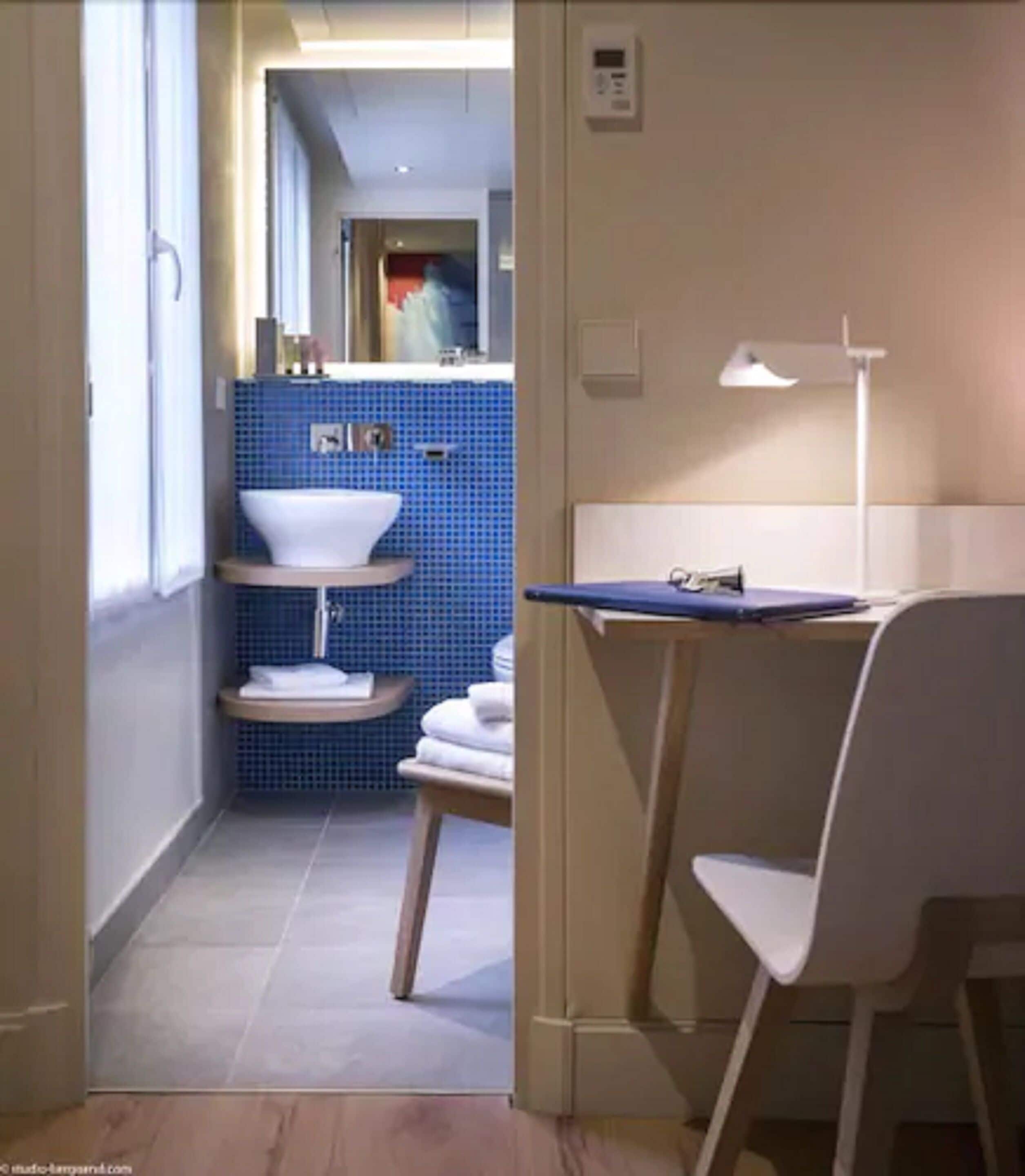 Un pasillo estrecho con un baño que tiene una pared con azulejos azules, un lavamanos blanco y un perchero para toallas.