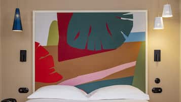 Une chambre d’hôtel avec un grand tableau abstrait au mur, un lit avec une literie blanche et jaune, une table de chevet et un téléphone.