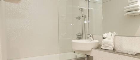 Ein modernes Badezimmer mit Duschkabine aus Glas, einem weißen Waschbecken und einer Toilette mit Handtuch darauf.