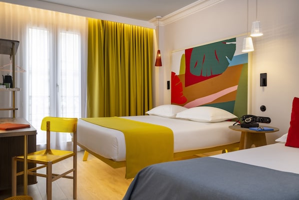 A hotel room with a bed, bedside table, chair, and a colorful abstract painting on the wall. - Hotel de la Paix (Paris)