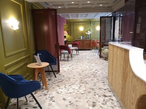 A hotel lobby with a reception desk, seating area with chairs, a patterned floor, and decorative elements. - Hotel de la Paix (Paris)