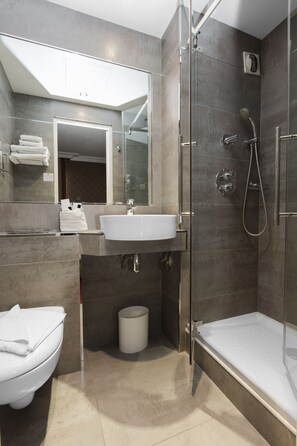 A modern bathroom with a glass-enclosed shower, a sink, and a toilet. - Hotel de la Paix (Paris)