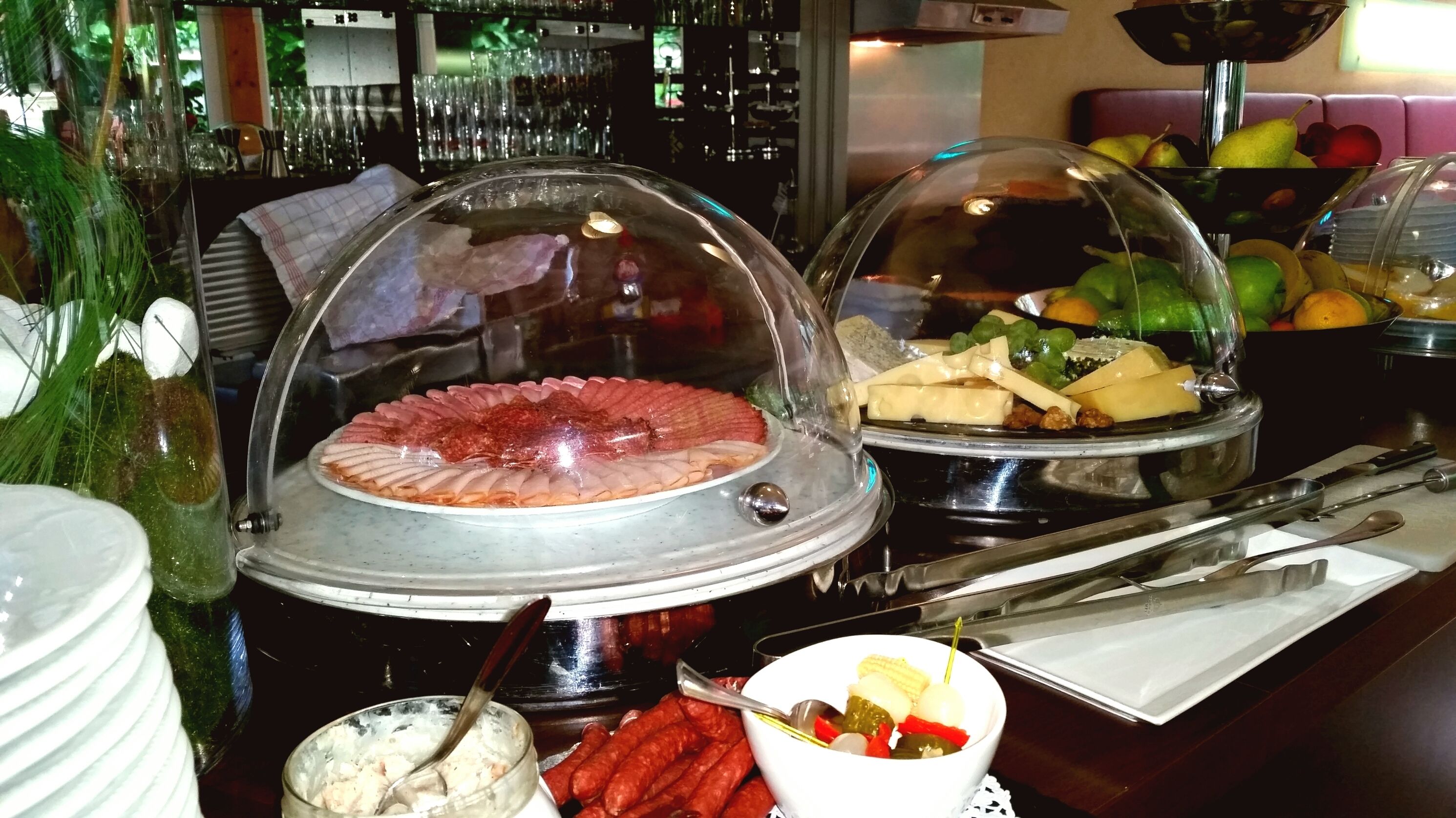 A buffet setup with covered food stations, including a variety of meats and a fruit bowl.
