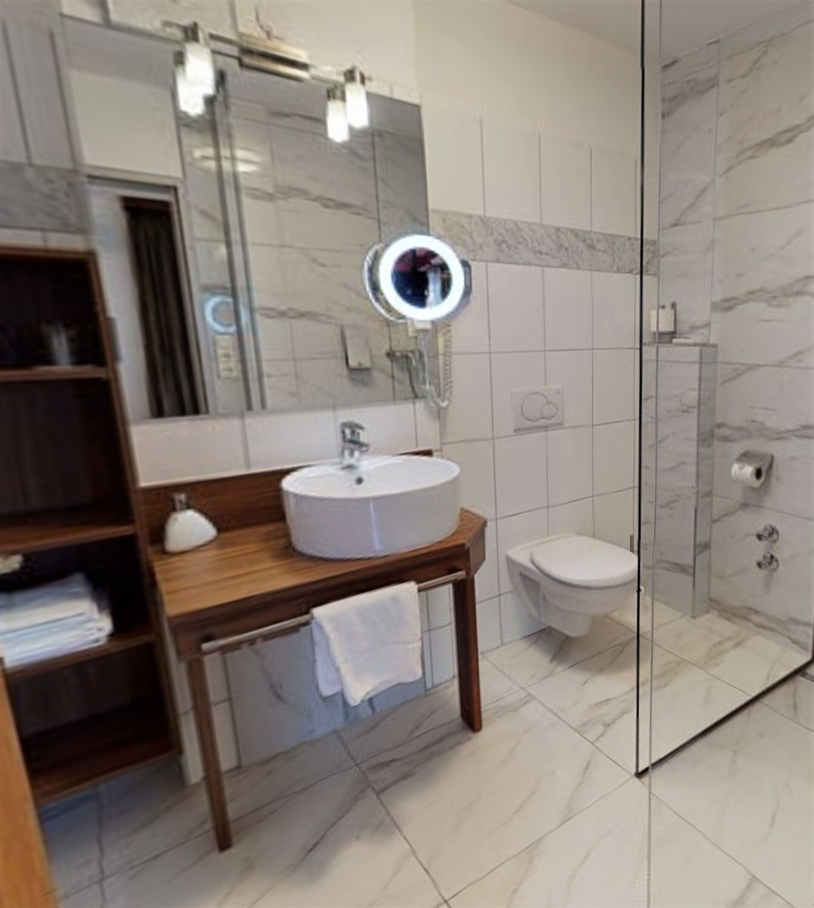 A modern bathroom with a round mirror, a sink, and a toilet.