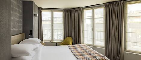 A hotel room with a large bed, a small round table, a chair, and a wall-mounted reading light.