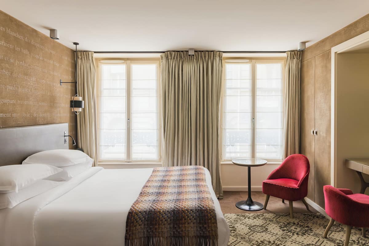 Une chambre d’hôtel avec un grand lit, une petite table, une chaise rouge et une vue par la fenêtre.