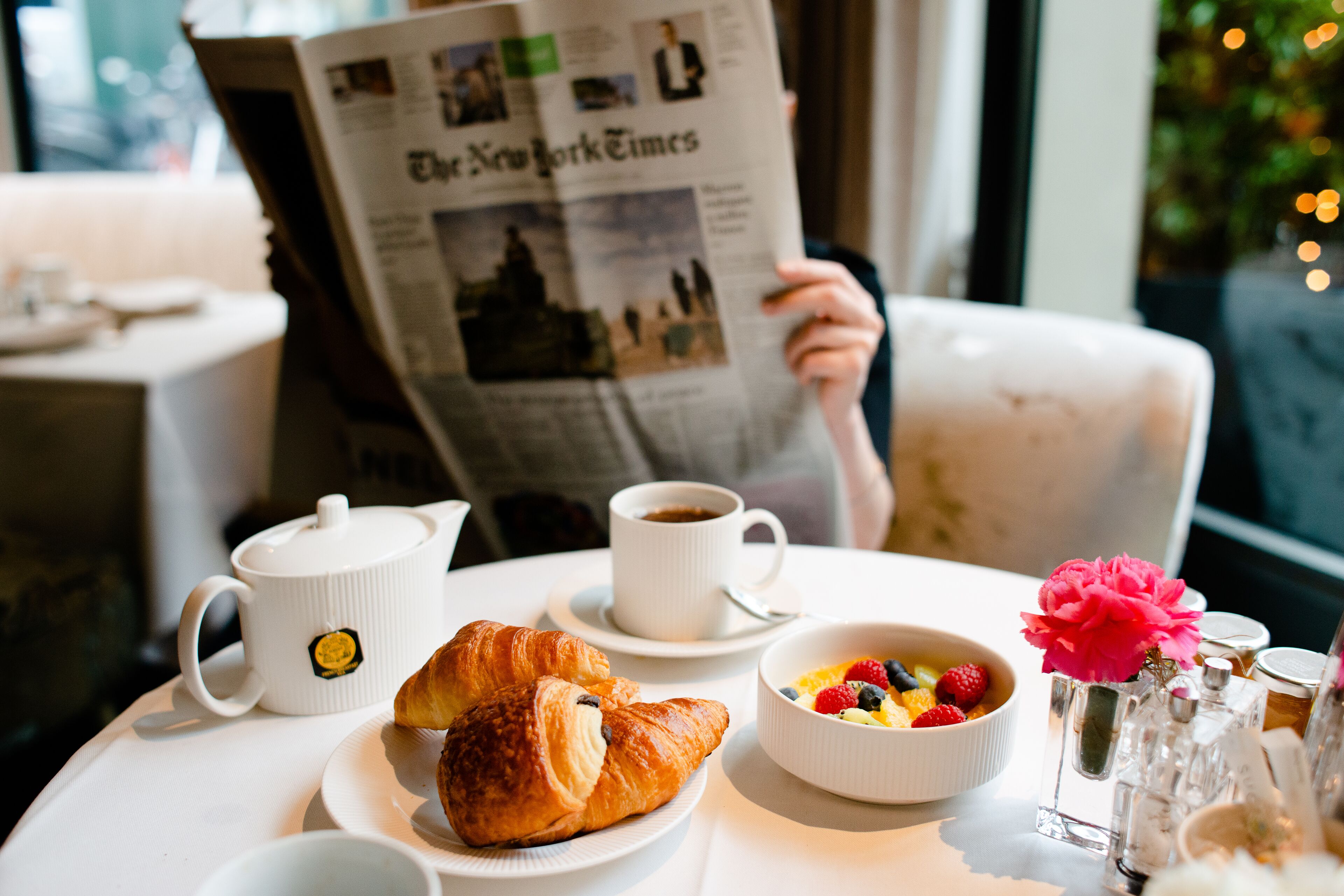 Un desayuno con cruasanes, un bol de fruta, café y un periódico.