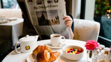 Un desayuno con cruasanes, un bol de fruta, café y un periódico.