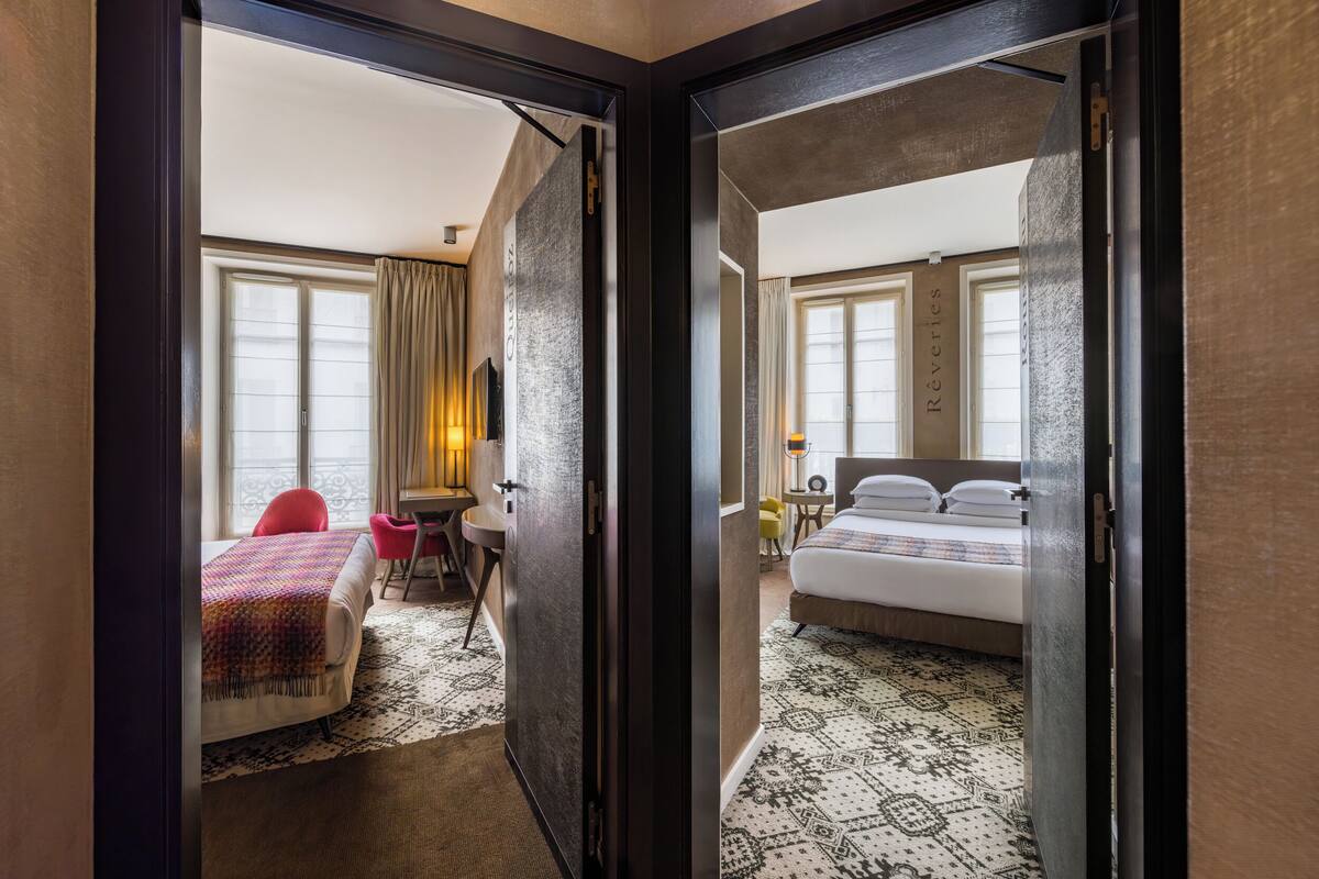 Une chambre d’hôtel avec un lit, un bureau et une chaise. Il y a une fenêtre avec des rideaux et une vue sur l’extérieur.