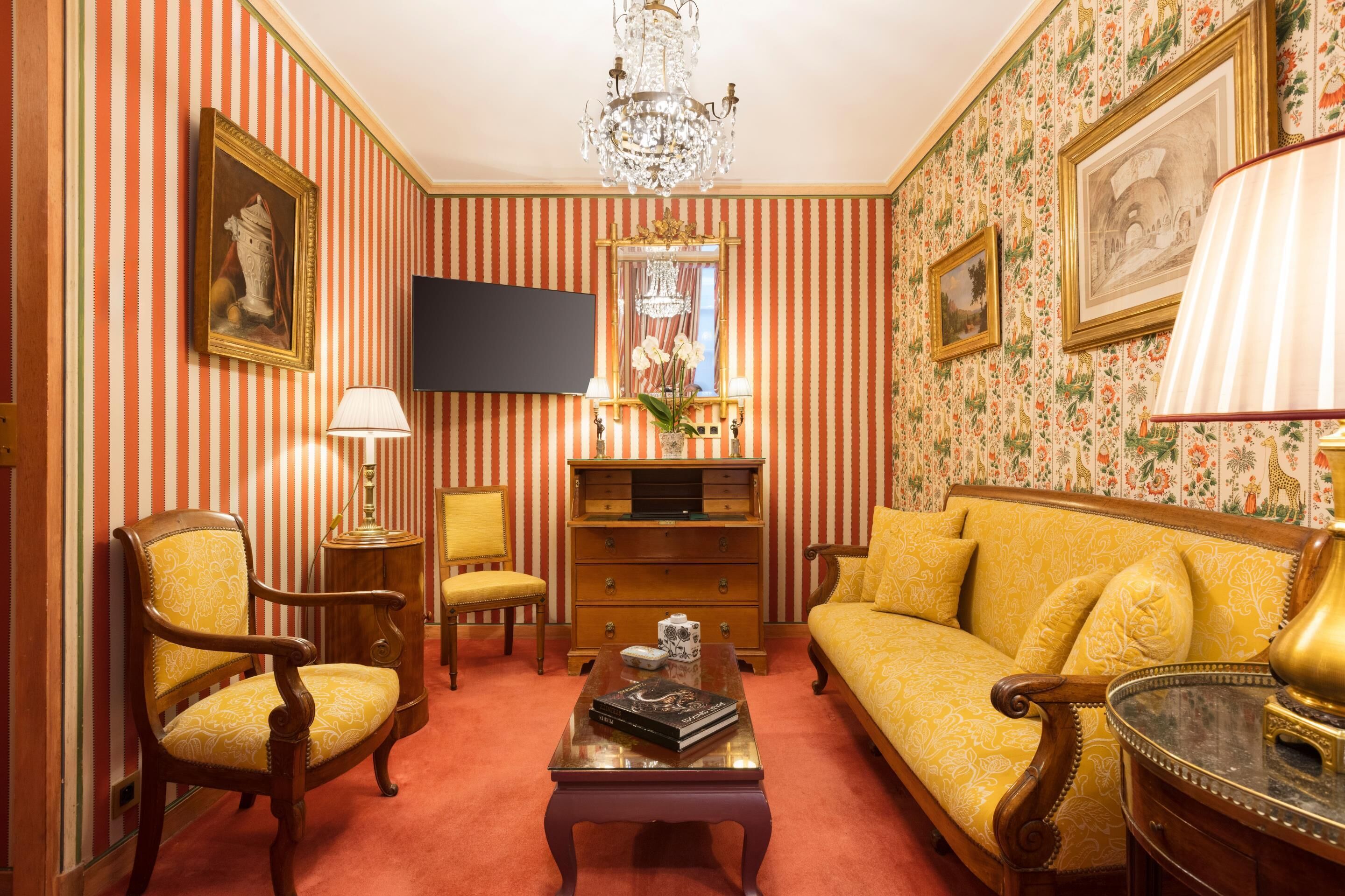Quarto com papel de parede listrado, um candelabro, um sofá, uma poltrona, uma mesa de centro e uma televisão de tela plana.