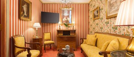 Quarto com papel de parede listrado, um candelabro, um sofá, uma poltrona, uma mesa de centro e uma televisão de tela plana.