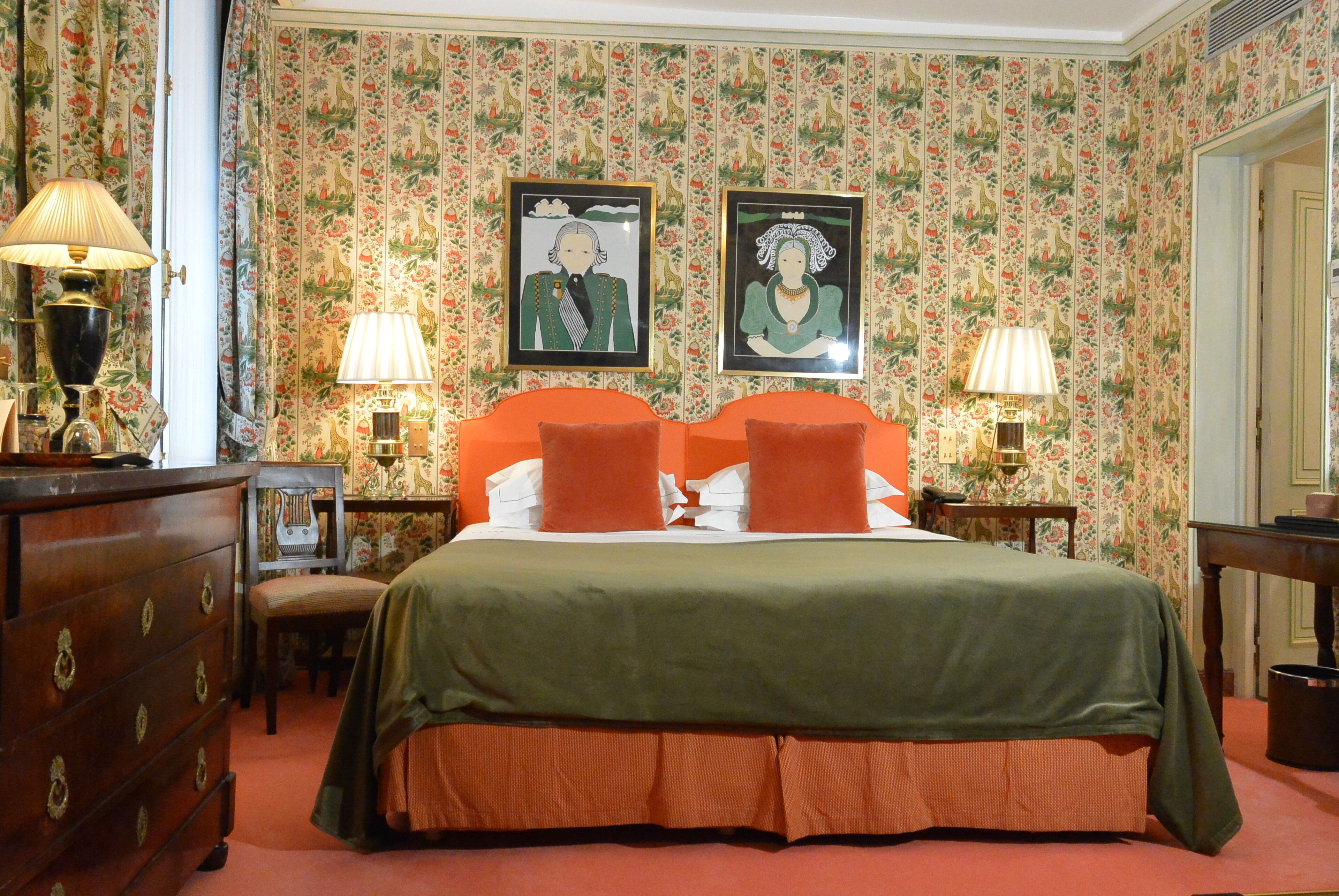 Habitación de hotel con una cama grande, dos mesitas de noche con lámparas, un aparador y papel tapiz con motivos florales.
