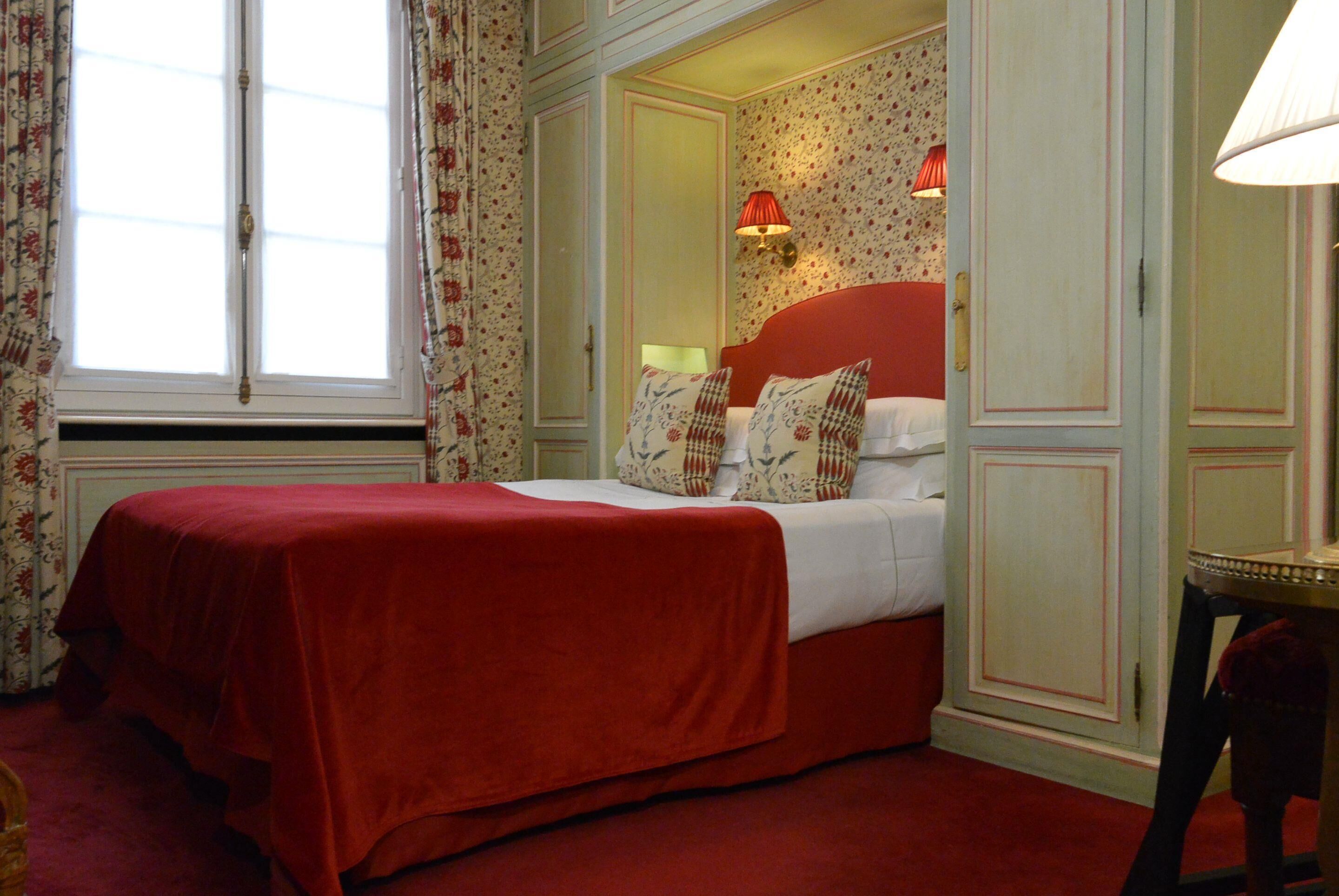 Un dormitorio con colcha roja, papel tapiz floral y cabecera roja.