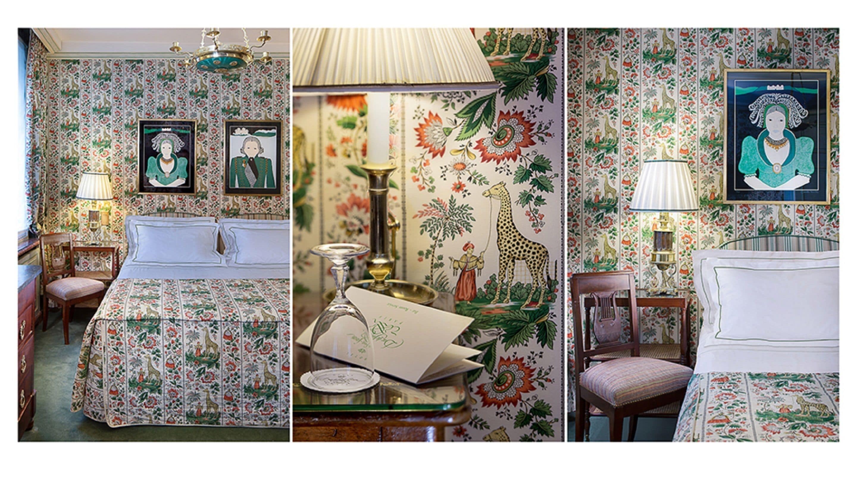A room with floral wallpaper, a bed with a matching headboard, a desk with a lamp, and framed artwork on the wall.