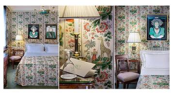 A room with floral wallpaper, a bed with a matching headboard, a desk with a lamp, and framed artwork on the wall.