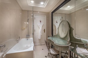 A luxurious bathroom with a large bathtub, a glass-enclosed vanity, and a large mirror.
