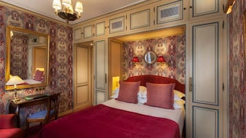 A hotel room with a large bed, a desk with a chair, a mirror, and a patterned wallpaper.