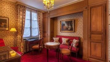 A room with a red carpet, wooden paneling, a red sofa with patterned cushions, a round wooden table, and a chandelier.