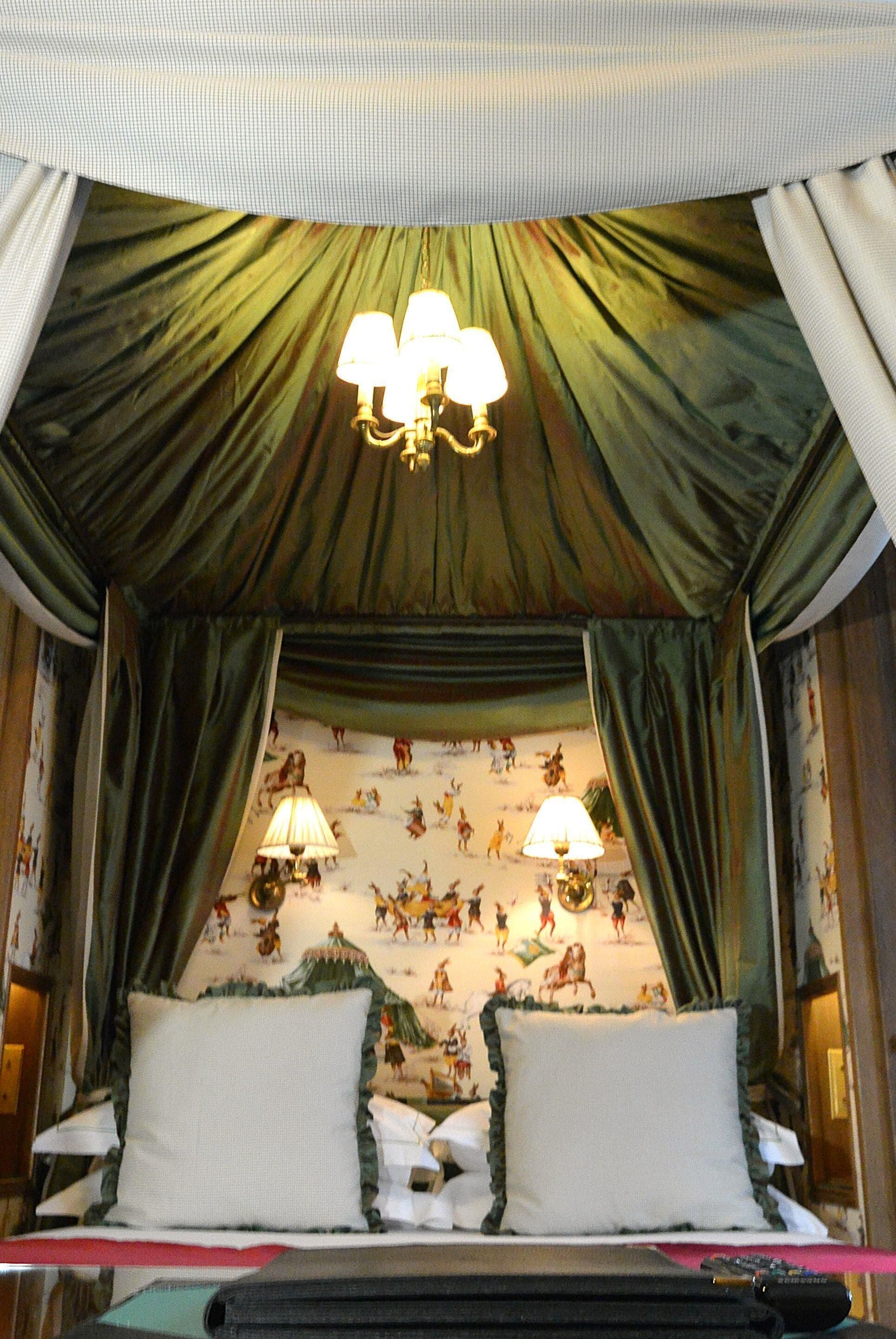 A bedroom with a canopy bed, two bedside lamps, and a mural of animals on the wall.