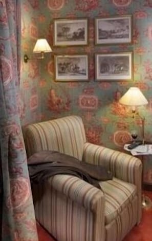 A room with a striped armchair, a table with a lamp, and framed pictures on the wall.