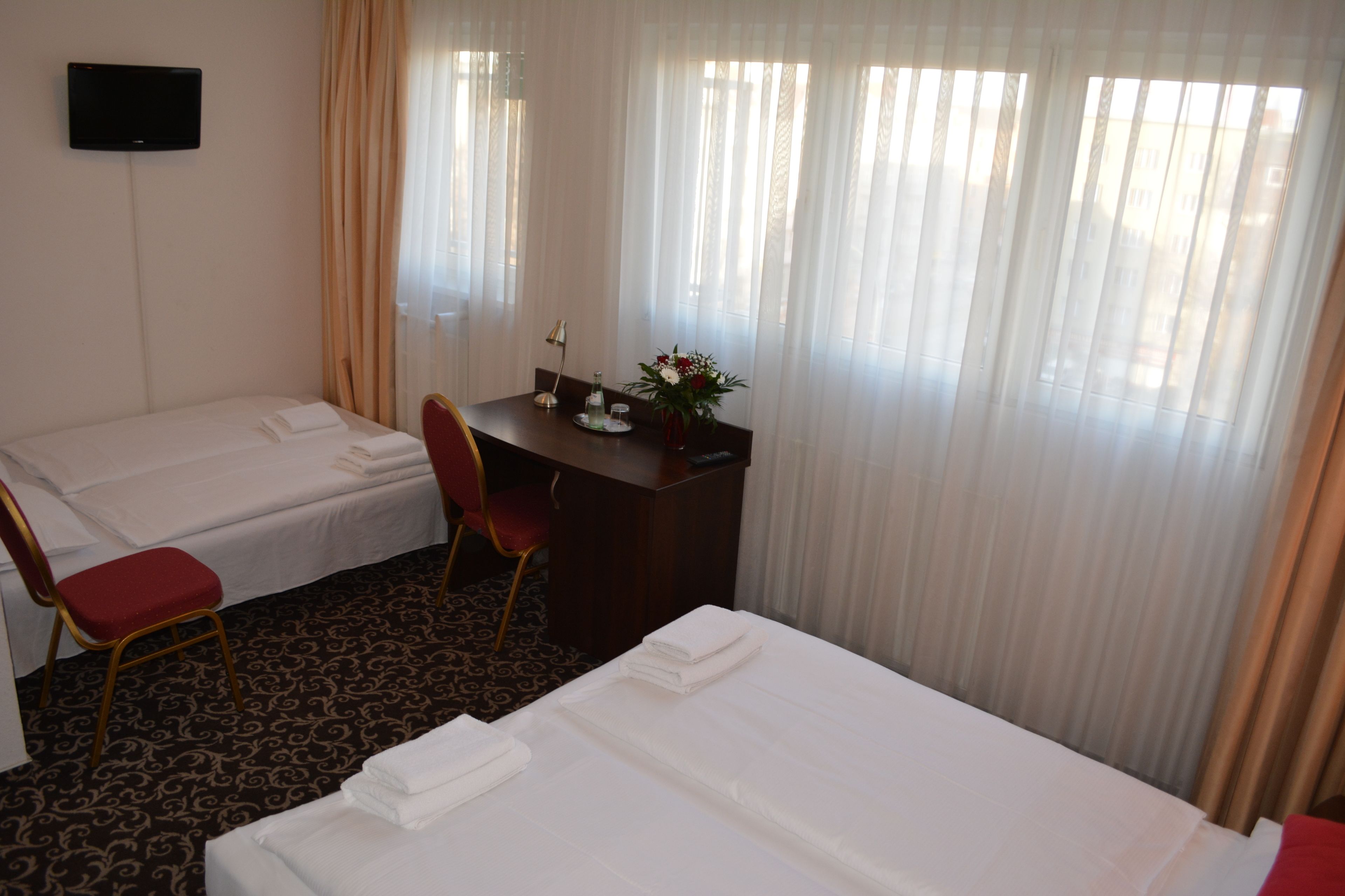 Habitación de hotel con dos camas, un escritorio, una silla, un televisor y una ventana con cortinas.