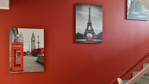 A red wall with three framed pictures: a red telephone booth, the Eiffel Tower, and a city street with a yellow taxi. - Hotel Atlas Berlin (Berlin)