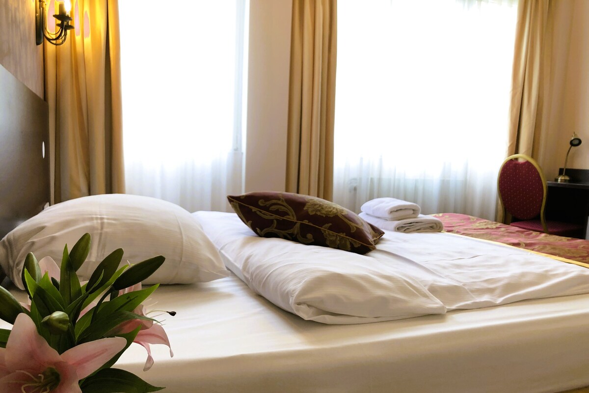 A neatly made bed with white linens, a decorative pillow, and a vase with flowers.