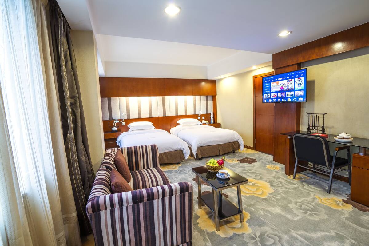 A hotel room with two beds, a sofa, a desk, a TV, and a coffee table.