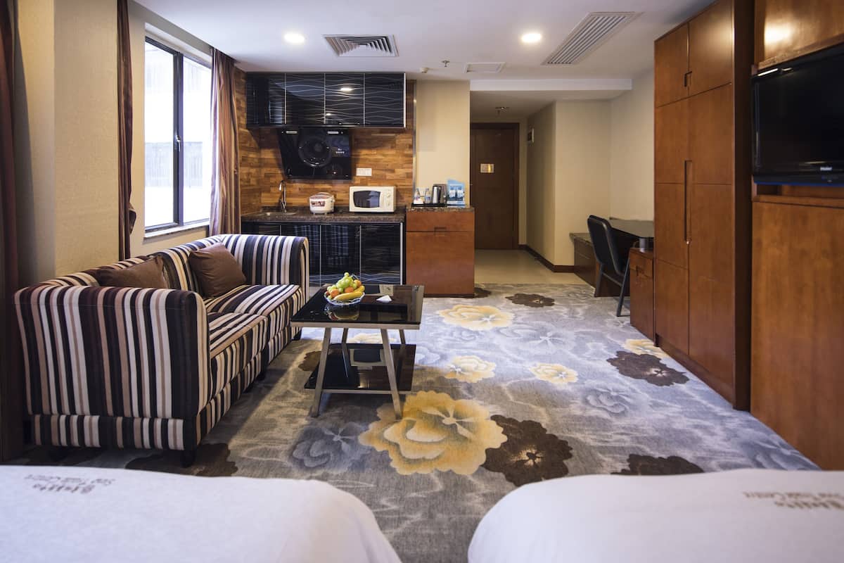 A compact hotel room with a sofa, a small table with a bowl of fruit, a microwave, and a television.