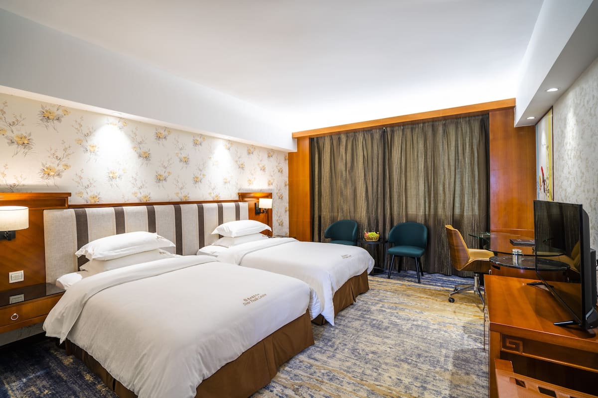 A hotel room with two beds, a desk, a chair, a television, and a bathroom area.