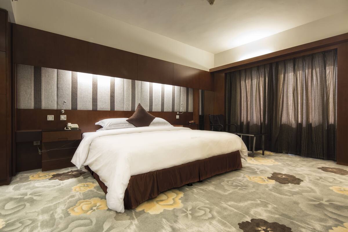 A hotel room with a large bed, a bedside table, a wardrobe, and a curtain.