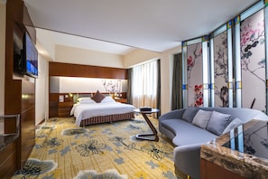 A hotel room with a bed, a sofa, a TV, and a decorative wall with floral patterns.