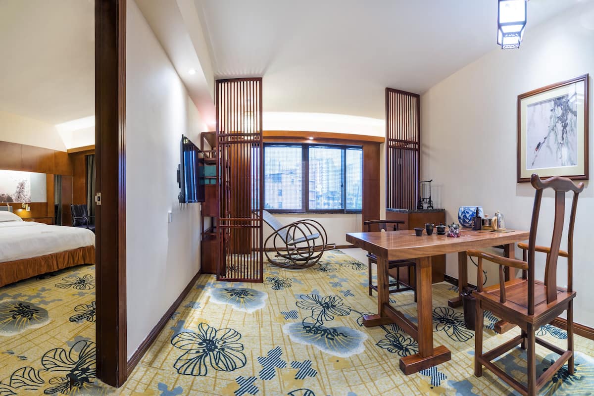 Habitación de hotel con cama, una mesa de comedor con sillas, un biombo decorativo y un ventanal con vistas a edificios.