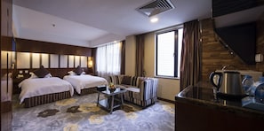 A hotel room with two beds, a sofa, a coffee table, a kitchen area with a kettle, and a large window with curtains.