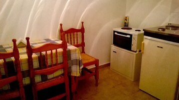 Una cocina compacta con una mesa de comedor, sillas, un microondas, un horno pequeño y un refrigerador.