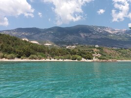 Un paisaje costero con aguas turquesas cristalinas, una playa arenosa y colinas verdes con edificios dispersos.
