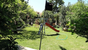 Un parque infantil con tobogán y estructura para escalar, rodeado de abundante vegetación.