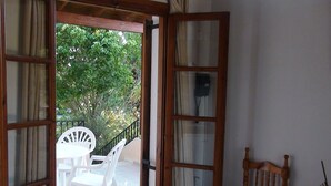 Puerta abierta que da a un balcón con una silla de plástico blanca y una silla de madera.