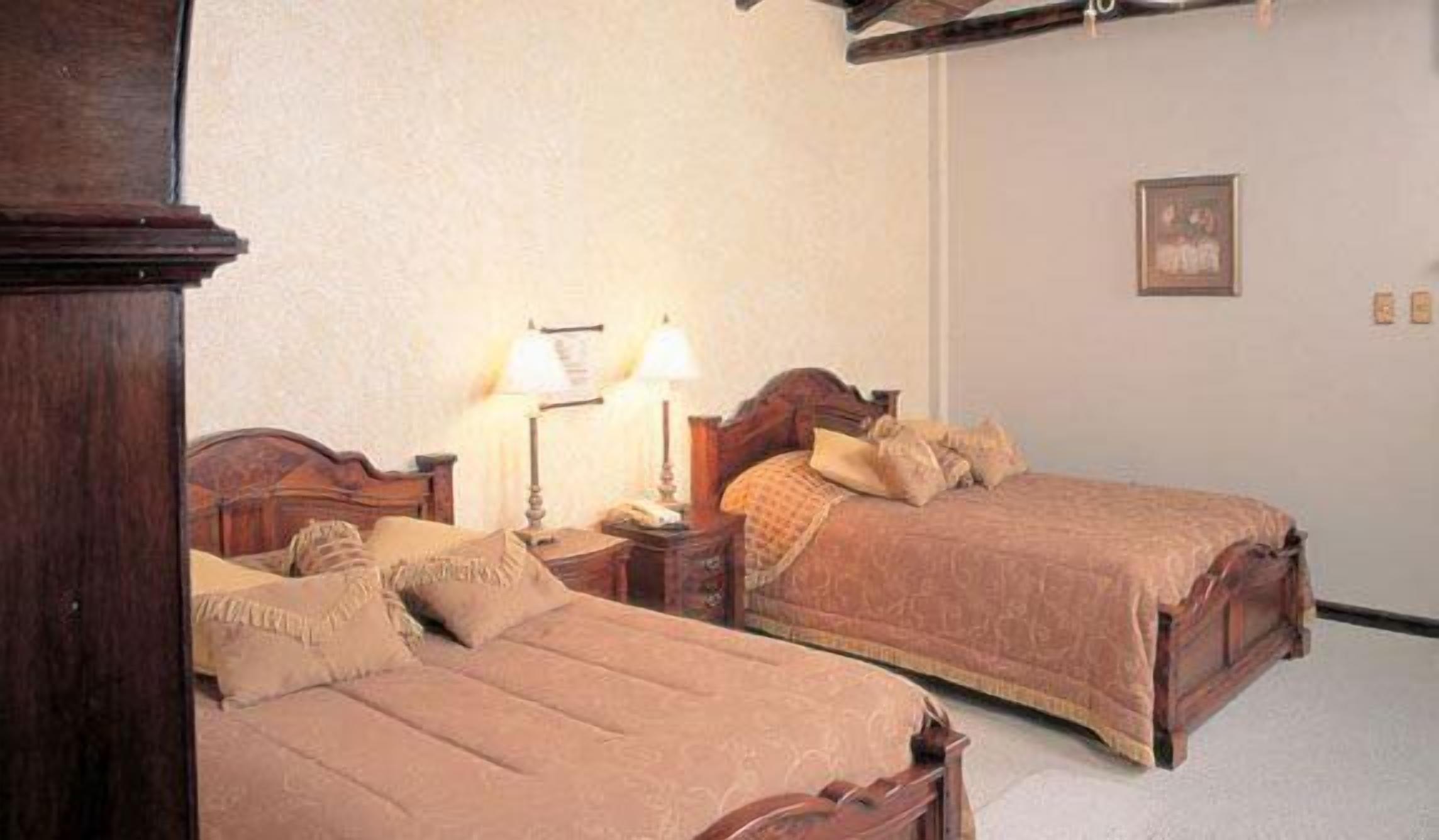Une chambre d’hôtel avec deux lits en bois, une table de chevet avec une lampe et un tableau encadré au mur.