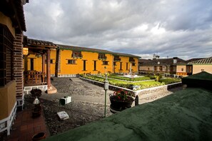 A courtyard with a fountain, potted plants, and a yellow building with balconies.