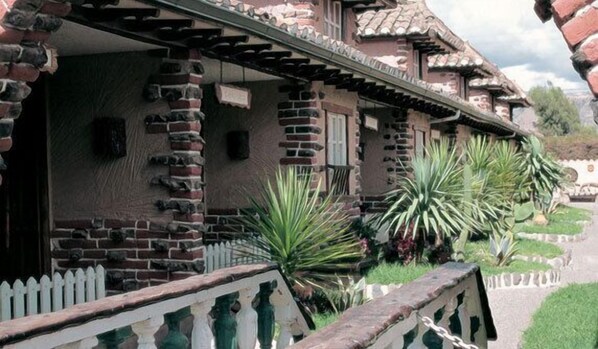 A traditional building with a brick facade, a white picket fence, and large green plants in front.