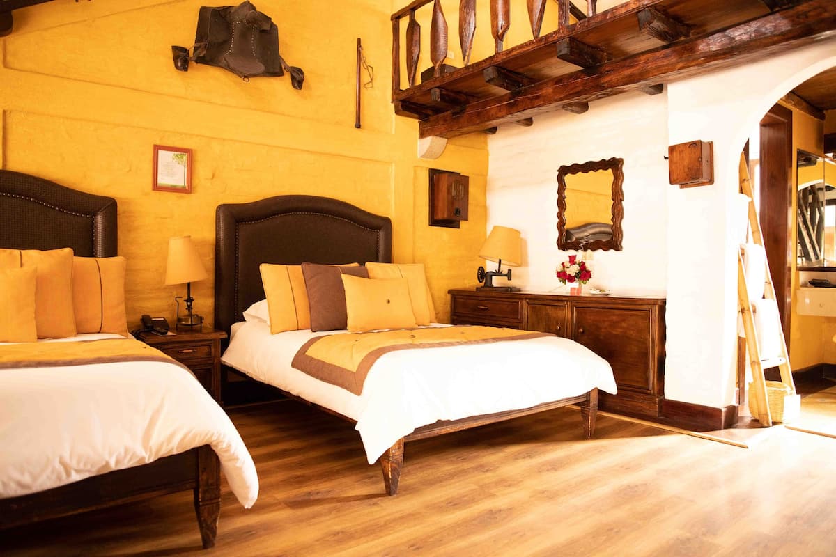 Ein Hotelzimmer mit zwei Betten, Holzböden, einem Holzkopfende, einem Nachttisch mit Lampe und einem Spiegel an der Wand.