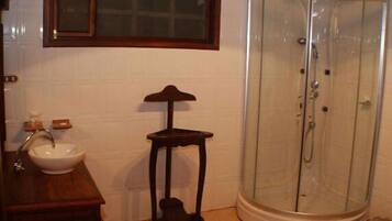 Un baño con lavabo, un taburete de madera y una cabina de ducha de vidrio.